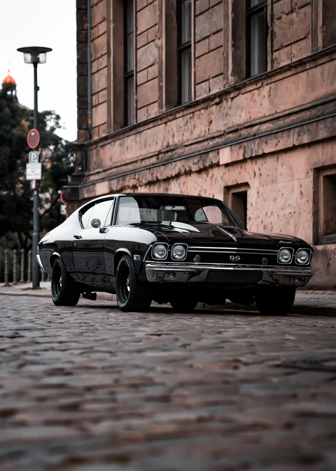 A classic dark muscle car on a cobbled street