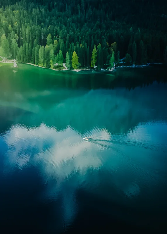 A lone boat reflected in a blue green lake surrounded by forest