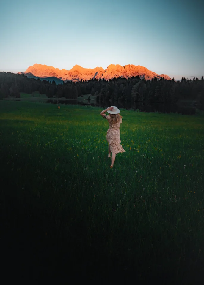 A figure in a meadow below mountains lit by the setting sun
